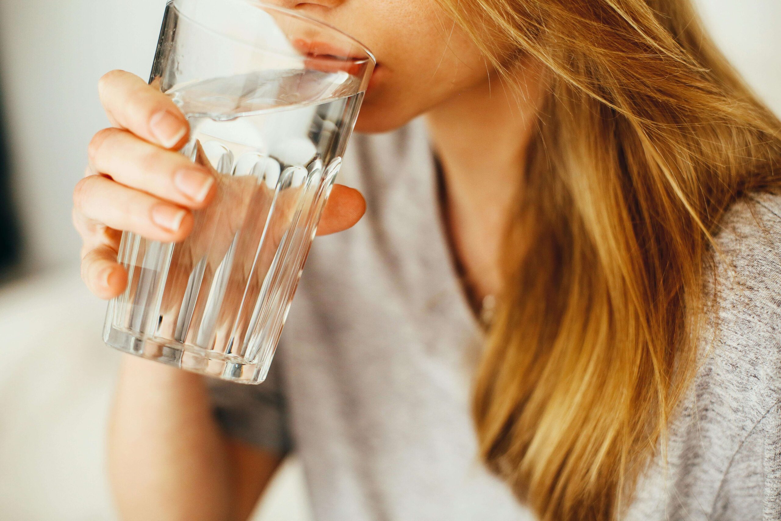 A woman drinking a glass of water to stay hydrated and healthy